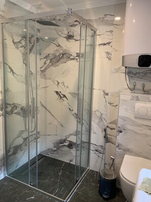 A glass-enclosed shower with a marble wall, a white toilet, and a handheld showerhead. - Vacation apartment in Montenegro. Quiet location near the sea. Welcome! (Bar)
