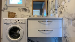 Un espace réduit dédié à la buanderie, comprenant un lave-linge, un miroir et une petite fenêtre.