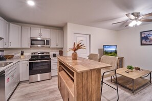 A modern kitchen with white cabinets, a built-in oven, and a dining area with a wooden table and chairs. - The Ruby 209 (Pigeon Forge)