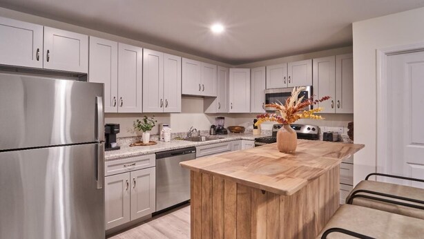 Een moderne keuken met witte kasten, roestvrijstalen apparatuur, een houten eiland en een vaas met gedroogde bloemen.