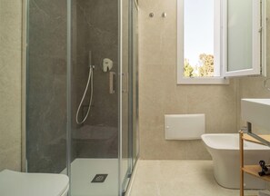 Ein modernes Badezimmer mit einer Duschkabine, einer weißen Toilette, einer freistehenden Badewanne und einem Fenster, das für natürliches Licht sorgt.