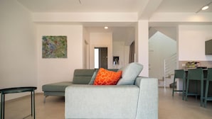 Una sala de estar moderna con un sofá gris, una mesita y una cocina al fondo.