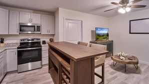 Eine Küche mit Mikrowelle, Herd und Weinkühlschrank, ein Essbereich mit Tisch und Stühlen, ein Deckenventilator und ein Fernseher auf einem Schrank.