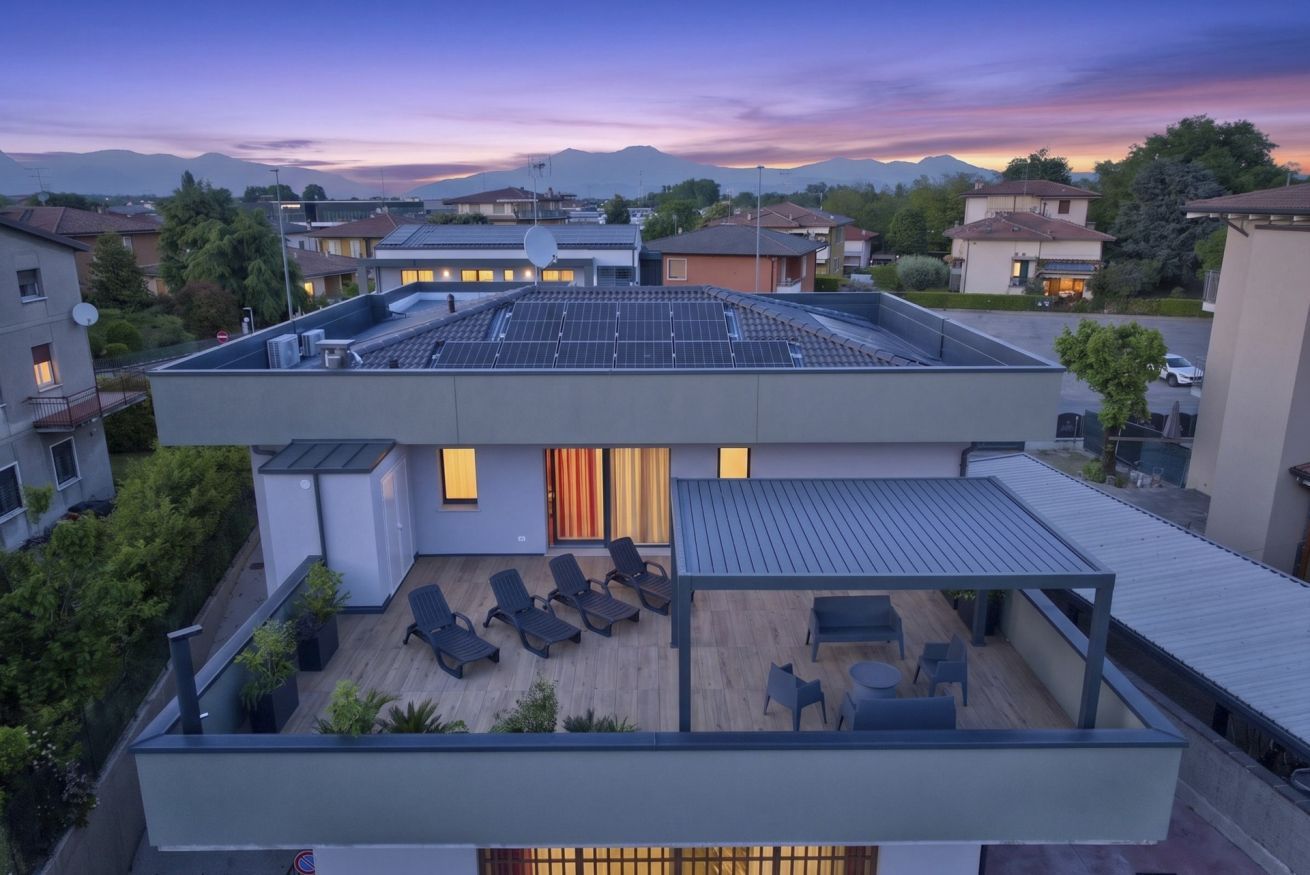 Un bâtiment moderne à deux étages, doté d’une terrasse sur le toit, de panneaux solaires et offrant une vue sur le quartier environnant.