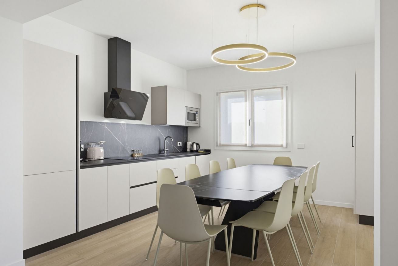 Una cocina moderna con una isla central, armarios blancos y un comedor con una mesa grande y sillas.