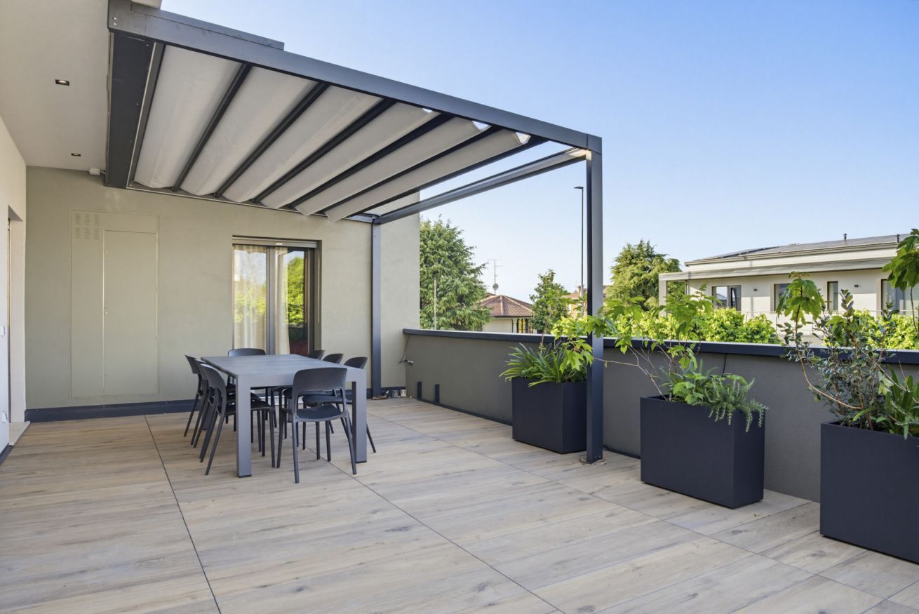 A covered outdoor area with a table and chairs, potted plants, and a view of neighboring buildings.