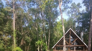 Una cabaña con terraza que da a un estanque, rodeada de un bosque denso.
