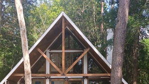 Una cabaña con terraza de madera, amplios ventanales y vistas al bosque circundante.