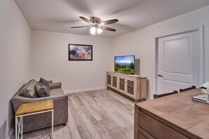 A living room with a sofa, TV, wooden cabinet, ceiling fan, and a door. - The Ruby 212 (Pigeon Forge)