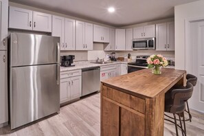 A modern kitchen with stainless steel appliances, white cabinetry, a wooden island, and bar stools. - The Ruby 213 (Pigeon Forge)