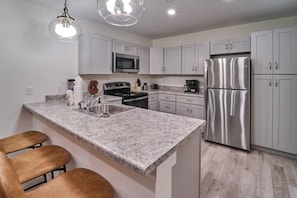 Una cocina moderna con encimeras de granito, electrodomésticos de acero inoxidable y una zona con taburetes de bar.