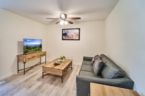 A living room with a sofa, a coffee table, a TV on a stand, a ceiling fan, and a framed picture on the wall. - The Ruby 300 (Pigeon Forge)