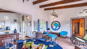 Amplia sala de estar con mesa de comedor lista para una comida, cocina al fondo y un rincón de descanso con una silla azul.