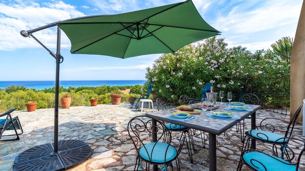 Un patio al aire libre con una mesa lista para comer, rodeada de sillas y una sombrilla que da sombra.