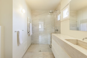 A modern bathroom with a glass-enclosed shower, a large mirror, and a beige marble countertop. - Golf Escape Villa by Cadenzalux (Sintra)