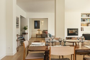 Un comedor con una mesa de madera preparada para cuatro personas, un sofá, una estantería y una chimenea.