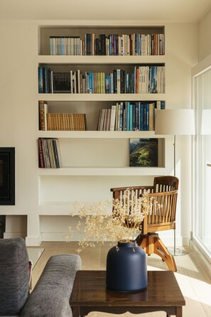A bookshelf with books, a wooden chair, a vase with dried flowers, and a lamp. - Golf Escape Villa by Cadenzalux (Sintra)