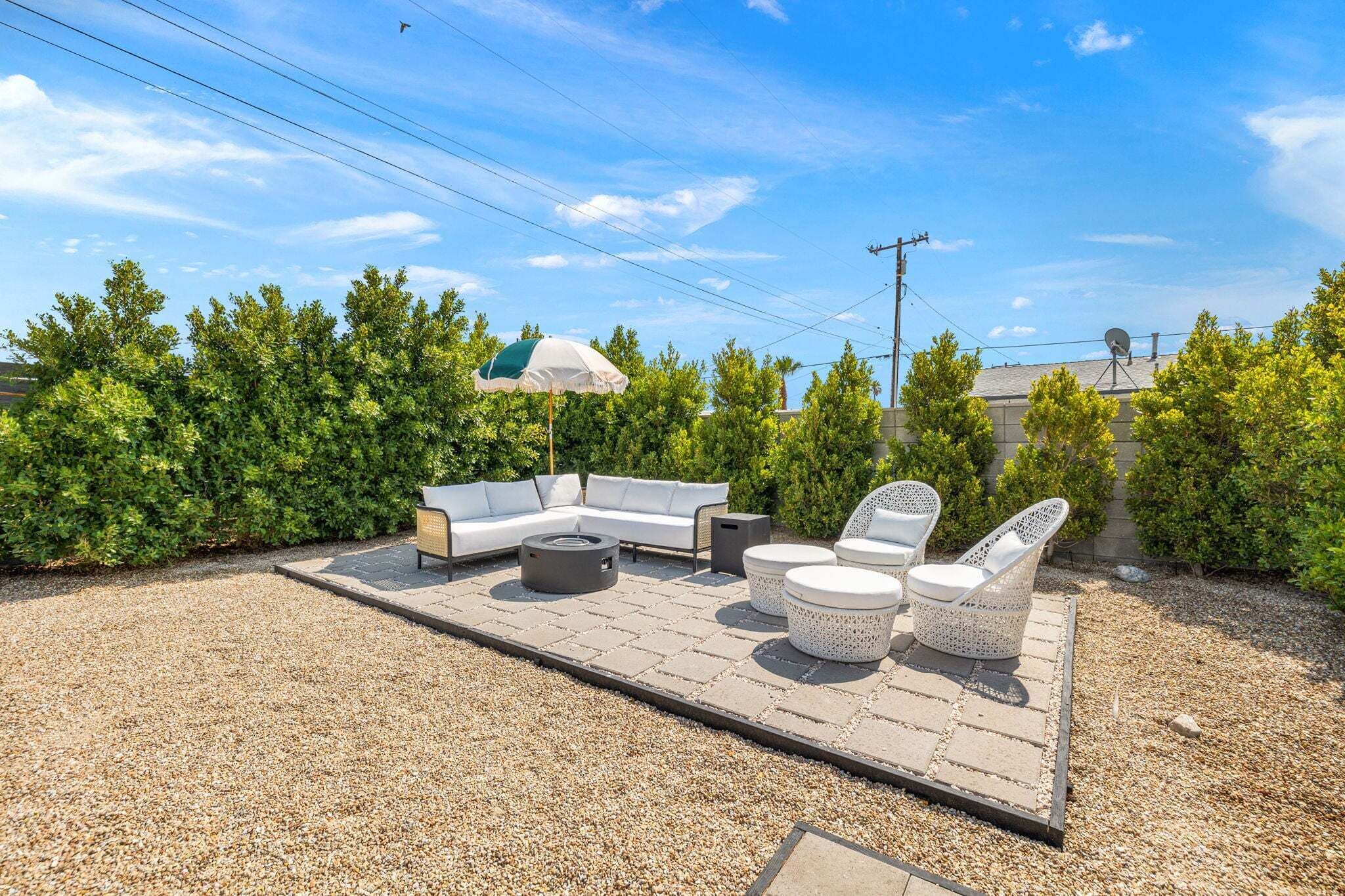 An outdoor patio area with a white sofa, two white chairs, a round table, and a small umbrella.