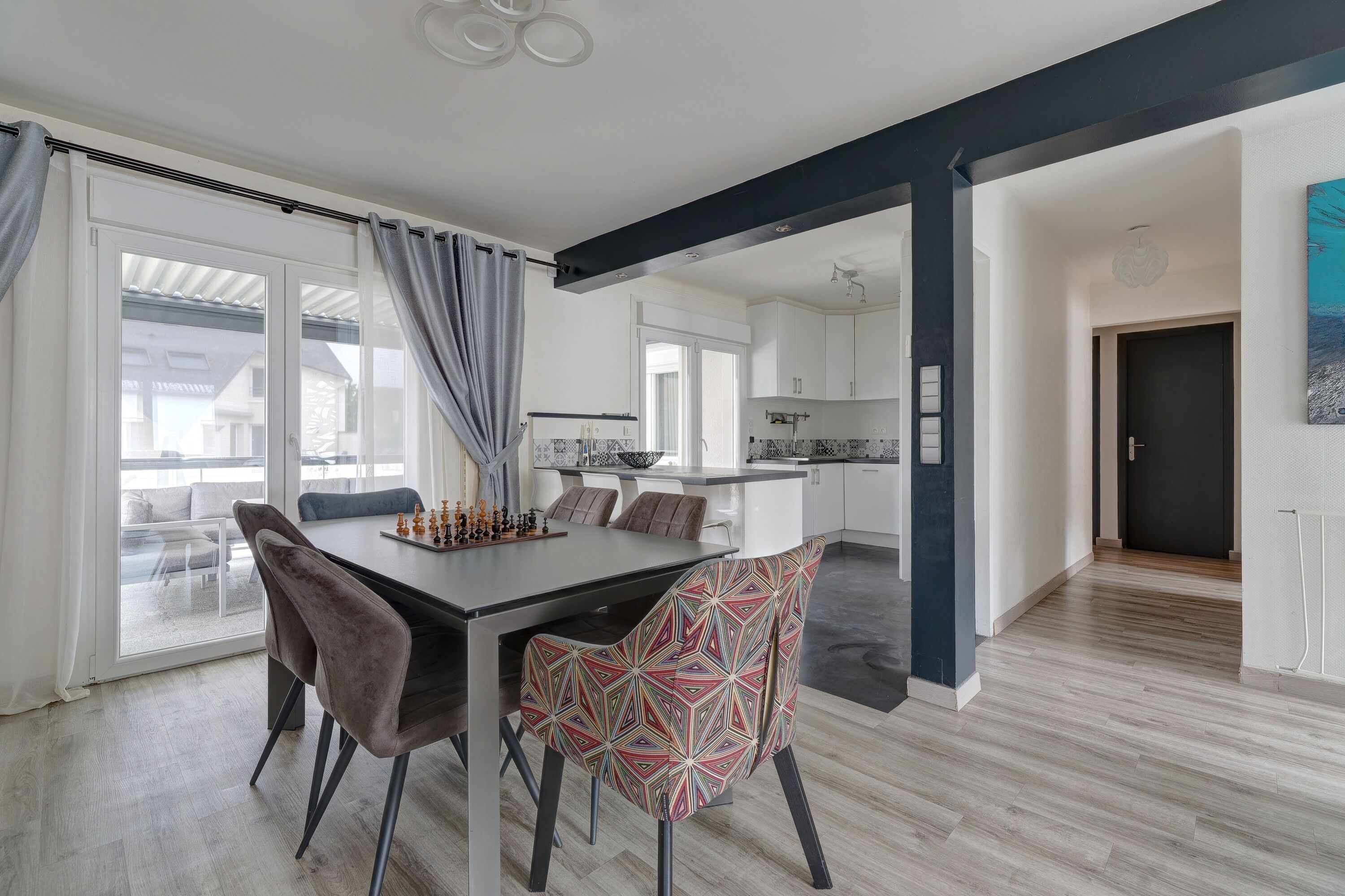 A modern kitchen with white cabinets, a dining area with a table and chairs, and a view through a glass door.