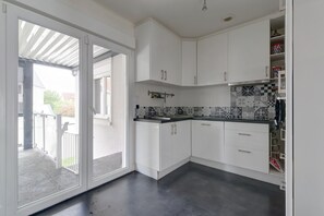 Une cuisine avec des meubles blancs, un plan de travail noir et un revêtement mural décoratif.
