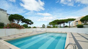 Une piscine dotée d’une terrasse carrelée, entourée d’arbres et de bâtiments.