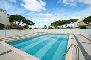 Ein Schwimmbecken mit gefliestem Sonnendeck, umgeben von Bäumen und Gebäuden.