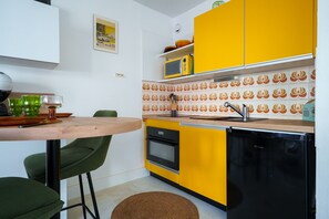Eine kompakte Küche mit Mikrowelle, Backofen und Spüle, einem kleinen Esstisch mit Stühlen und einer gestreiften Spritzschutzwand.