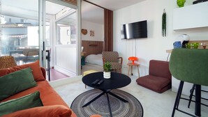Un salon moderne avec un canapé, une table basse ronde, un téléviseur fixé au mur et une porte-fenêtre coulissante donnant sur un balcon.