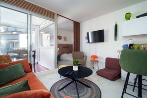 Ein modernes Wohnzimmer mit einer Couch, einem runden Couchtisch, einem an der Wand montierten Fernseher und einer Glastür zum Balkon.