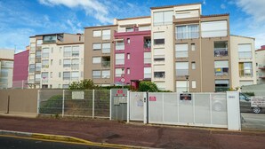 Un immeuble résidentiel à plusieurs étages, doté de balcons, d’une entrée sécurisée et surplombant un ciel dégagé.