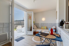 Ein kompakter Raum mit einem Bett, einem kleinen Tisch, einer Küchenzeile und einer Schiebetür zu einem Sitzbereich im Freien.