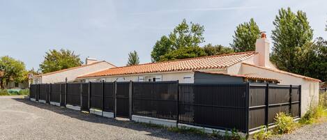 A building with a tiled roof, a fenced area, and a gravel driveway.