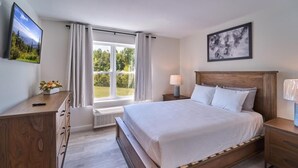 A bedroom with a bed, a wooden dresser, a nightstand, a lamp, a picture on the wall, and a window with curtains. - The Ruby 302 (Pigeon Forge)