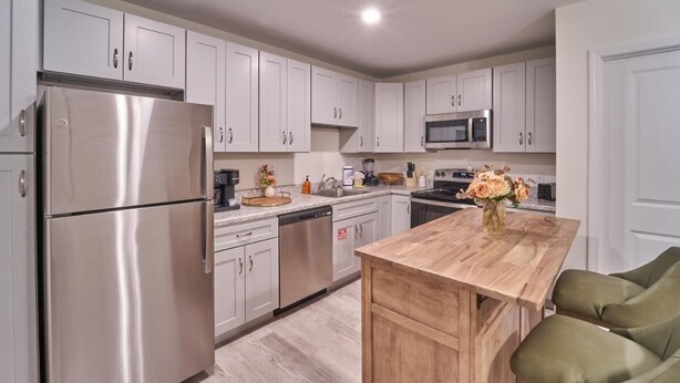 A modern kitchen with white cabinets, stainless steel appliances, a wooden dining table, and green upholstered chairs. - The Ruby 302 (Pigeon Forge)