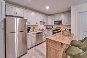 A modern kitchen with white cabinets, stainless steel appliances, a wooden dining table, and green upholstered chairs. - The Ruby 302 (Pigeon Forge)