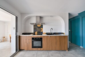 A modern kitchen with wooden cabinets, a built-in oven, a stainless steel range hood, and a patterned backsplash. - Le Cara - Situé en front de mer (La Turballe)