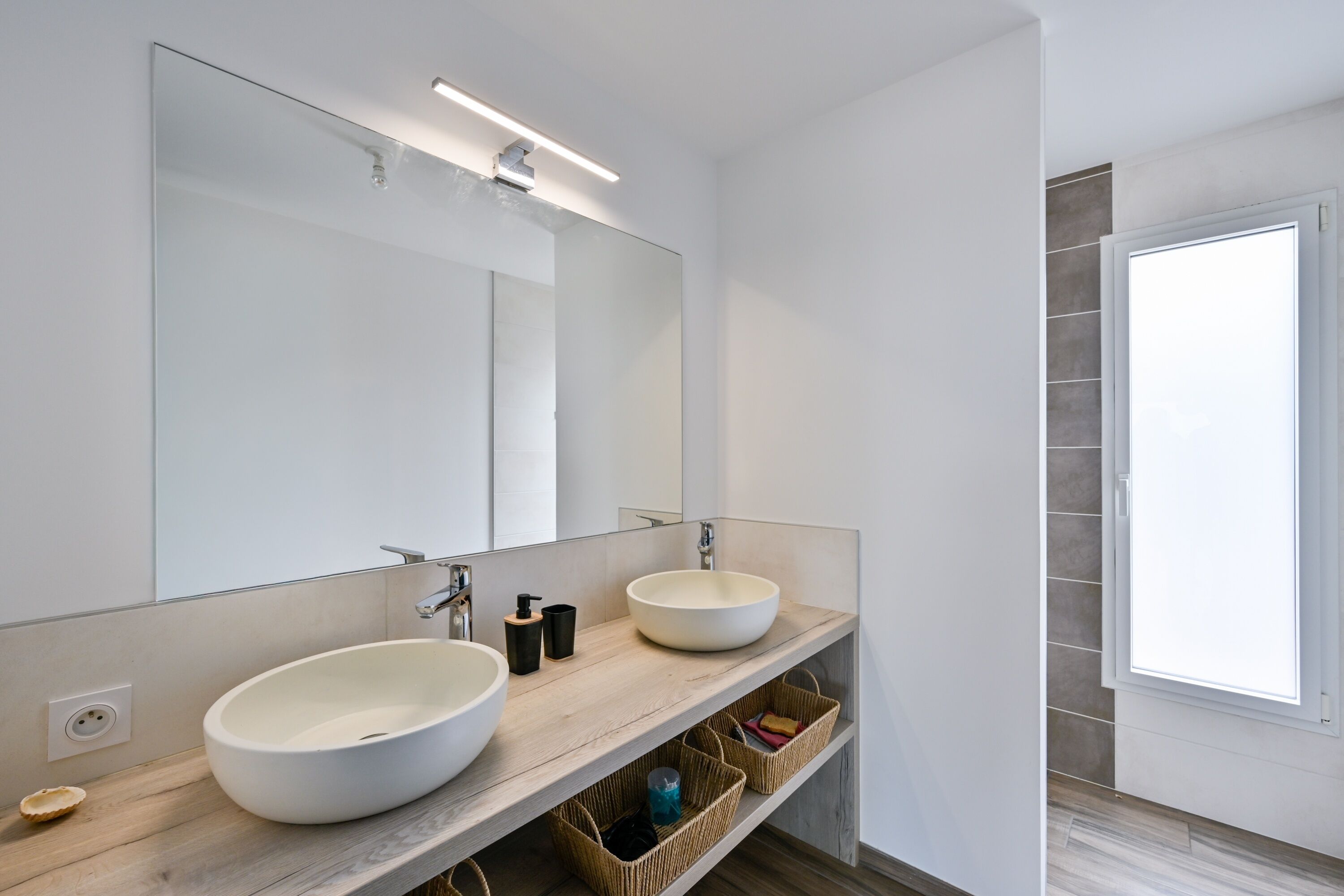 A modern bathroom with two large sinks, a mirror, and a window.