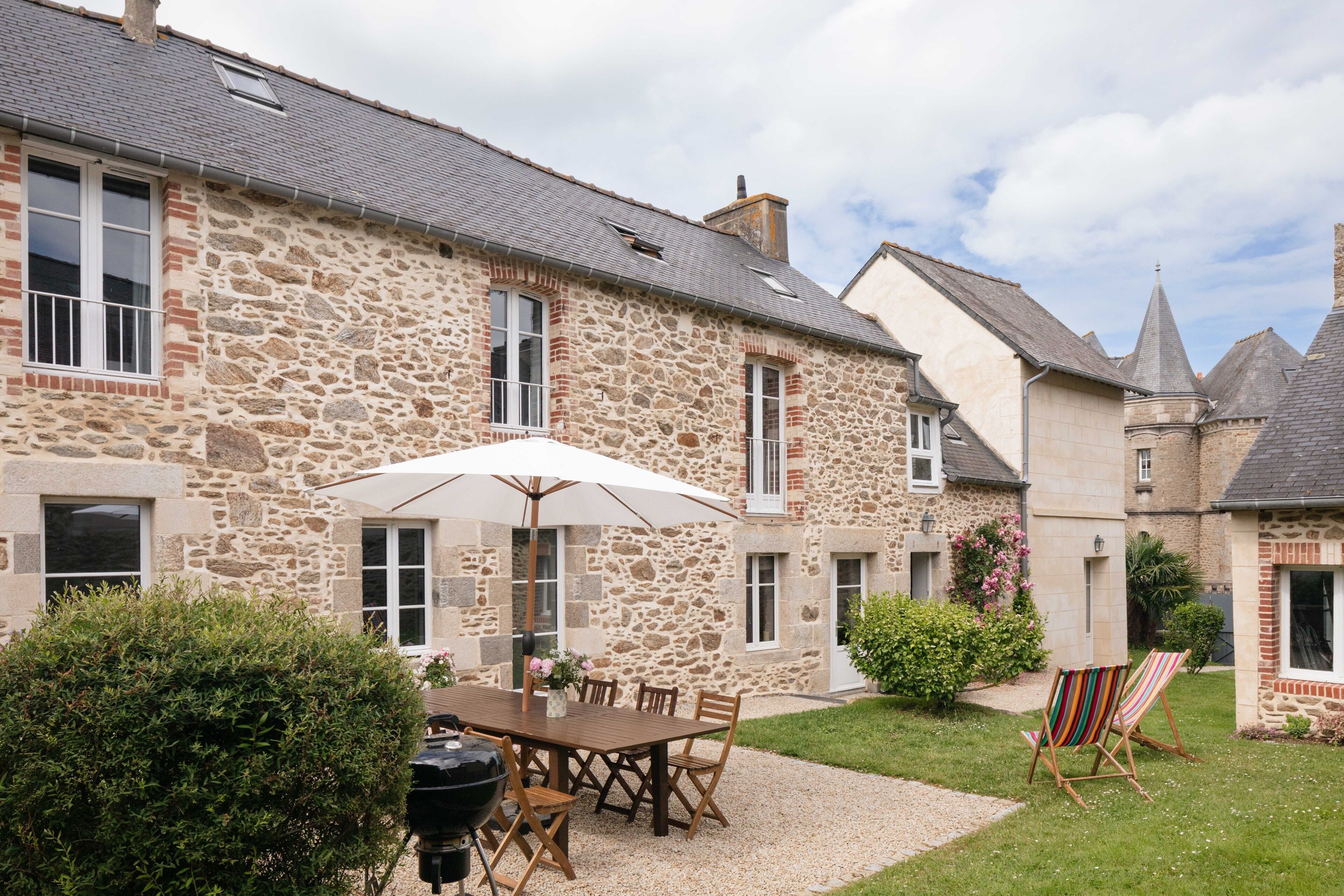 A stone building with a patio area featuring a table, chairs, and a grill.