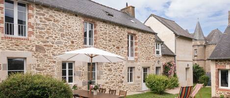A stone building with a patio area featuring a table, chairs, and a grill.