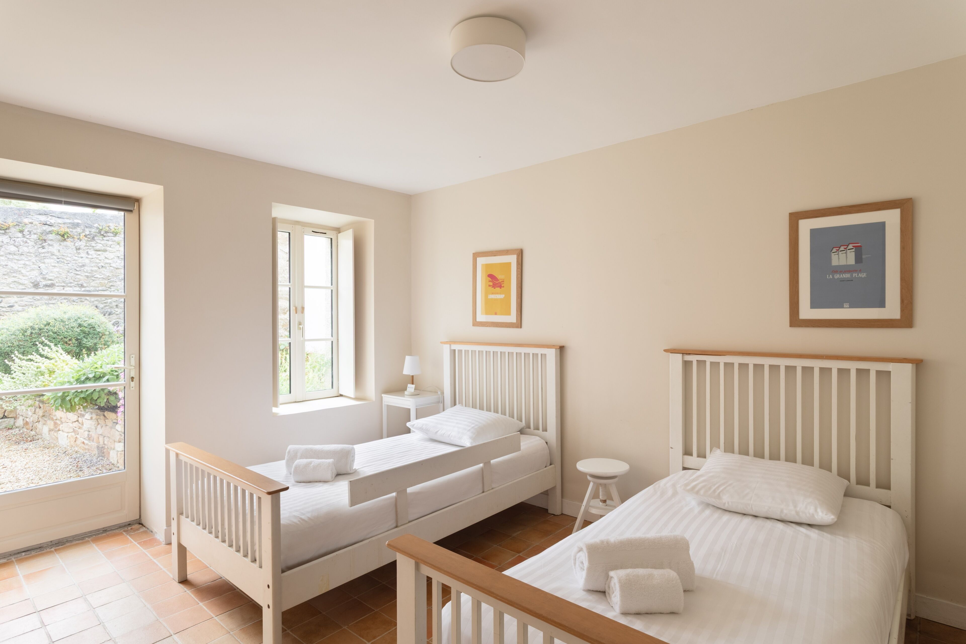 A bedroom with two beds, a window, a bedside table, and a framed picture on the wall.