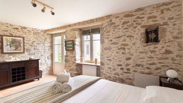 Una camera da letto con pareti in pietra, un letto con lenzuola bianche, un comò di legno e una finestra vista.