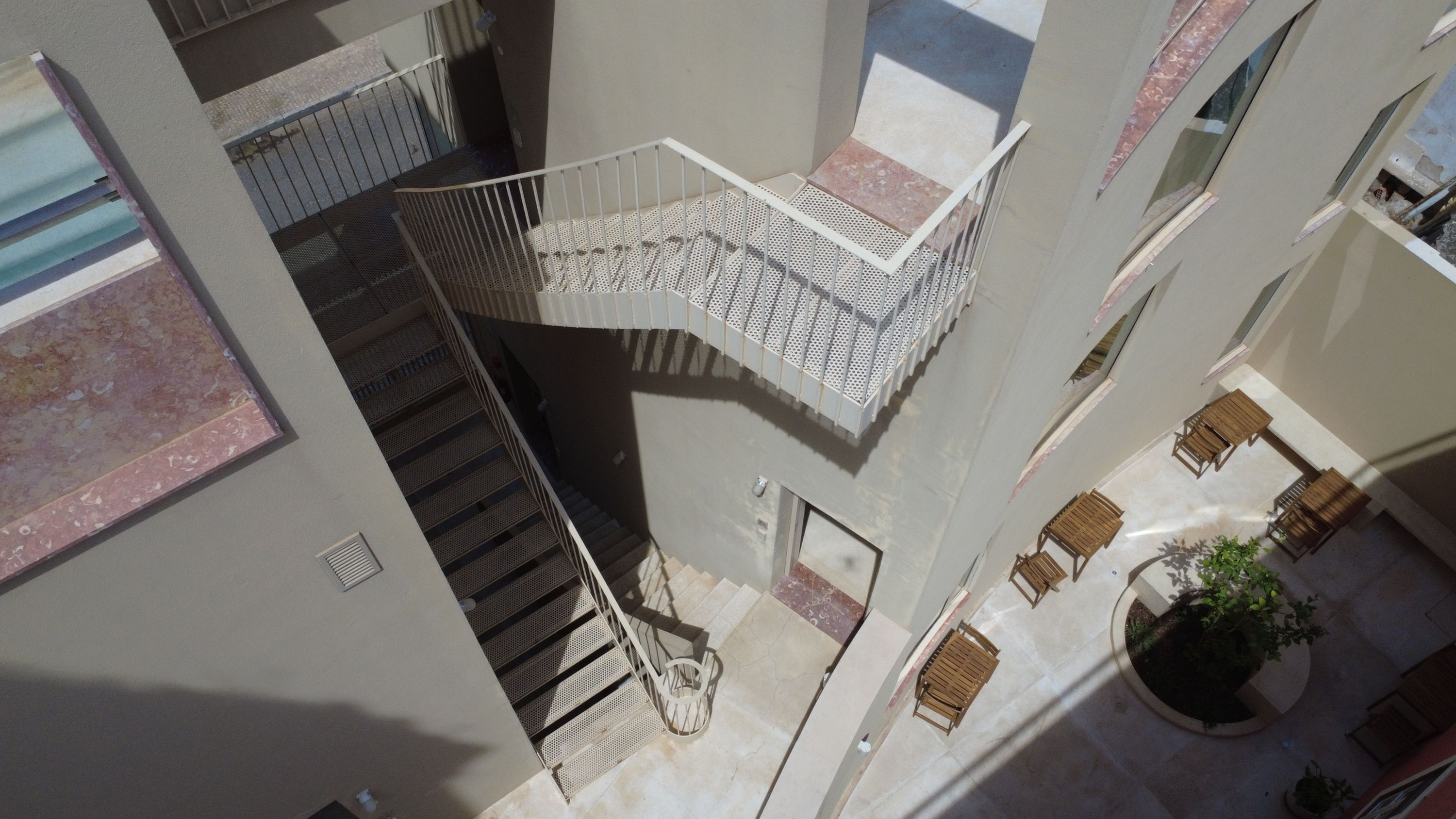 Un edificio de varios niveles con una escalera central, zona de estar exterior y una jardinera circular.