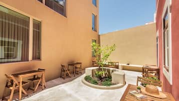 An outdoor seating area with wooden tables and chairs, a small garden, and a building with large windows.