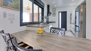Una cucina moderna con un tavolo da pranzo in legno, sedie, un cesto di frutta, un'ampia finestra e una porta che dà su un'altra stanza.
