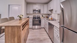 A modern kitchen with stainless steel appliances, a wooden dining table, and light-colored cabinetry. - The Ruby 304 (Pigeon Forge)