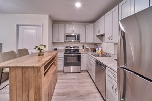 A modern kitchen with stainless steel appliances, a wooden dining table, and light-colored cabinetry. - The Ruby 304 (Pigeon Forge)