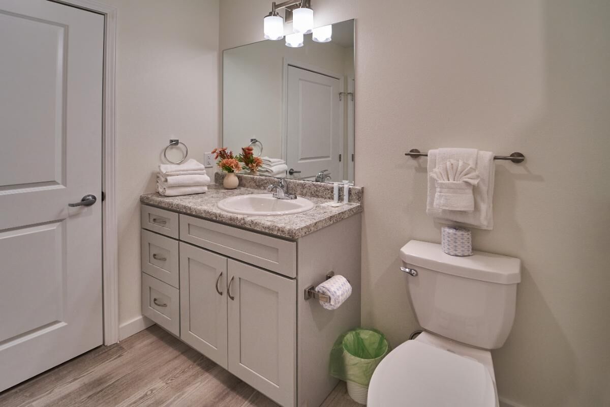 Une salle de bain équipée d’un lavabo, d’un miroir, de toilettes et d’une poubelle.