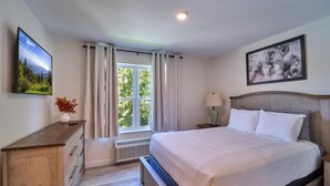 Une chambre à coucher comprenant un lit, une table de chevet, une commode, une fenêtre avec des rideaux et un tableau accroché au mur.