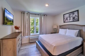 Quarto com cama, mesa de cabeceira, cômoda, janela com cortinas e um quadro na parede.