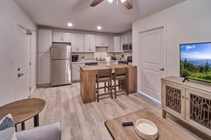 A modern kitchen with white cabinets, a stainless steel refrigerator, a wooden dining table, and a TV on a wooden cabinet. - The Ruby 306 (Pigeon Forge)